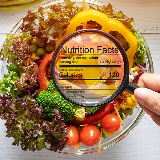 nutritional information concept. hand use the magnifying glass to zoom in to see the details of the nutrition facts from food , salad bowl